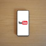 Top view of smartphone displaying YouTube logo on a wooden surface, showcasing modern technology.