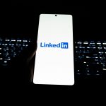Close-up of LinkedIn logo on smartphone with backlit keyboard in dark room.