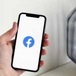 Close-up of a hand holding a smartphone displaying the Facebook logo indoors.